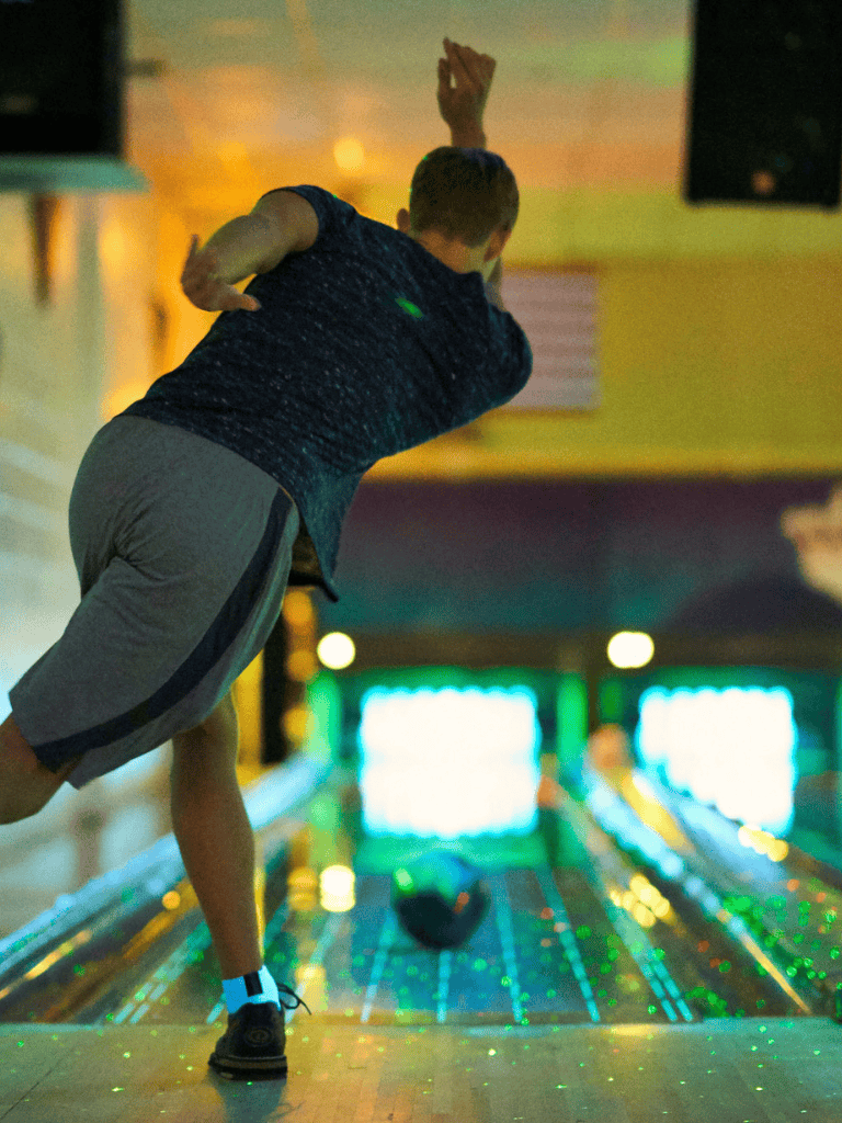 Indoor bowling alley with colorful lighting and a child throwing a bowling ball.