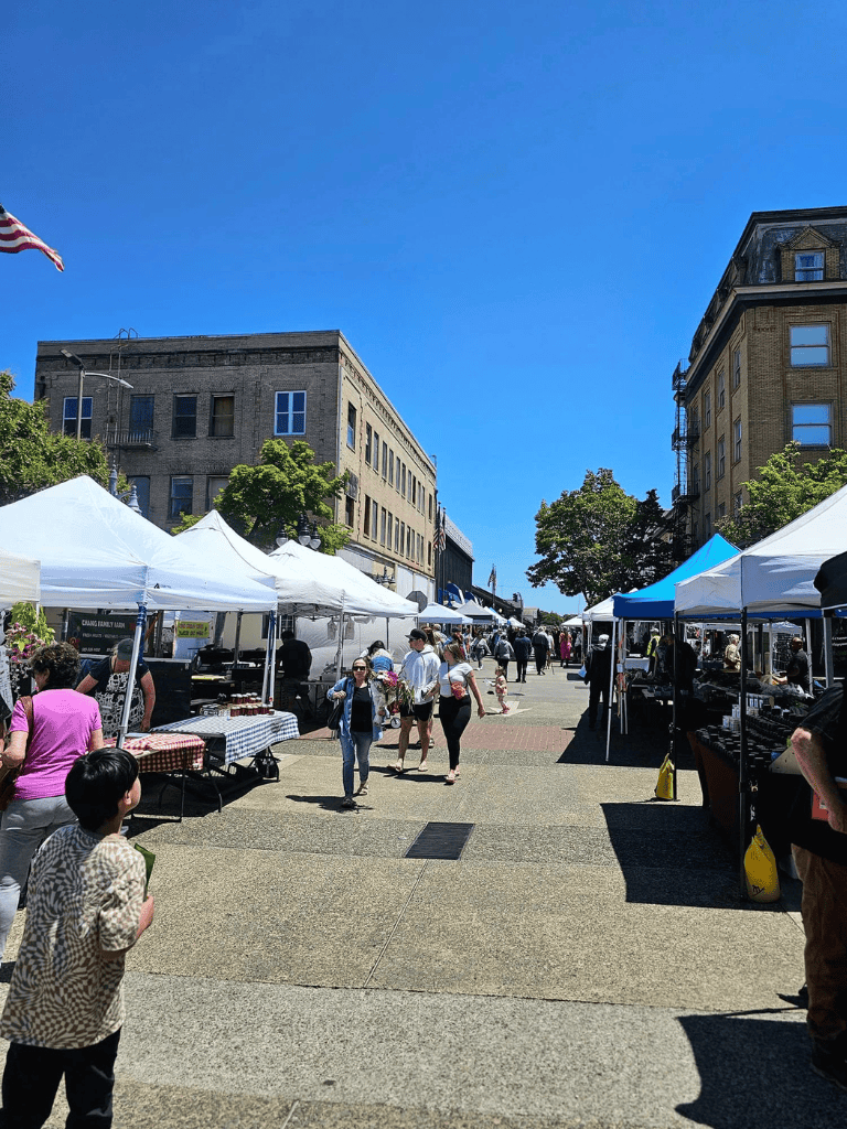 Vibrant outdoor market with tents and people shopping on a sunny day in downtown.