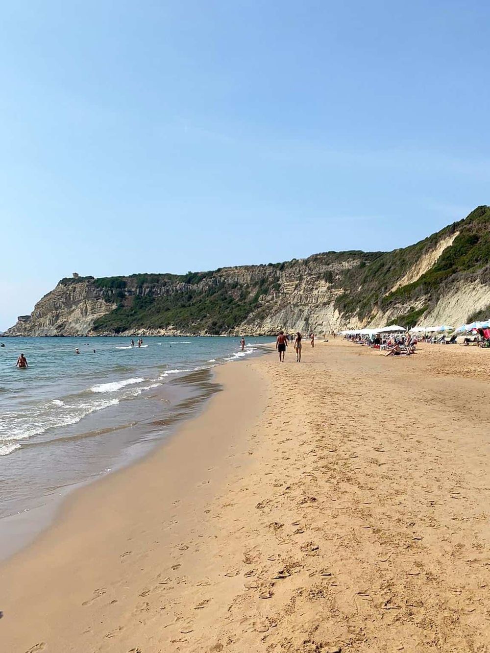 Stunning beach with golden sand, rugged cliffs, and people enjoying the seaside scenery. Ideal for travel and vacation planning.