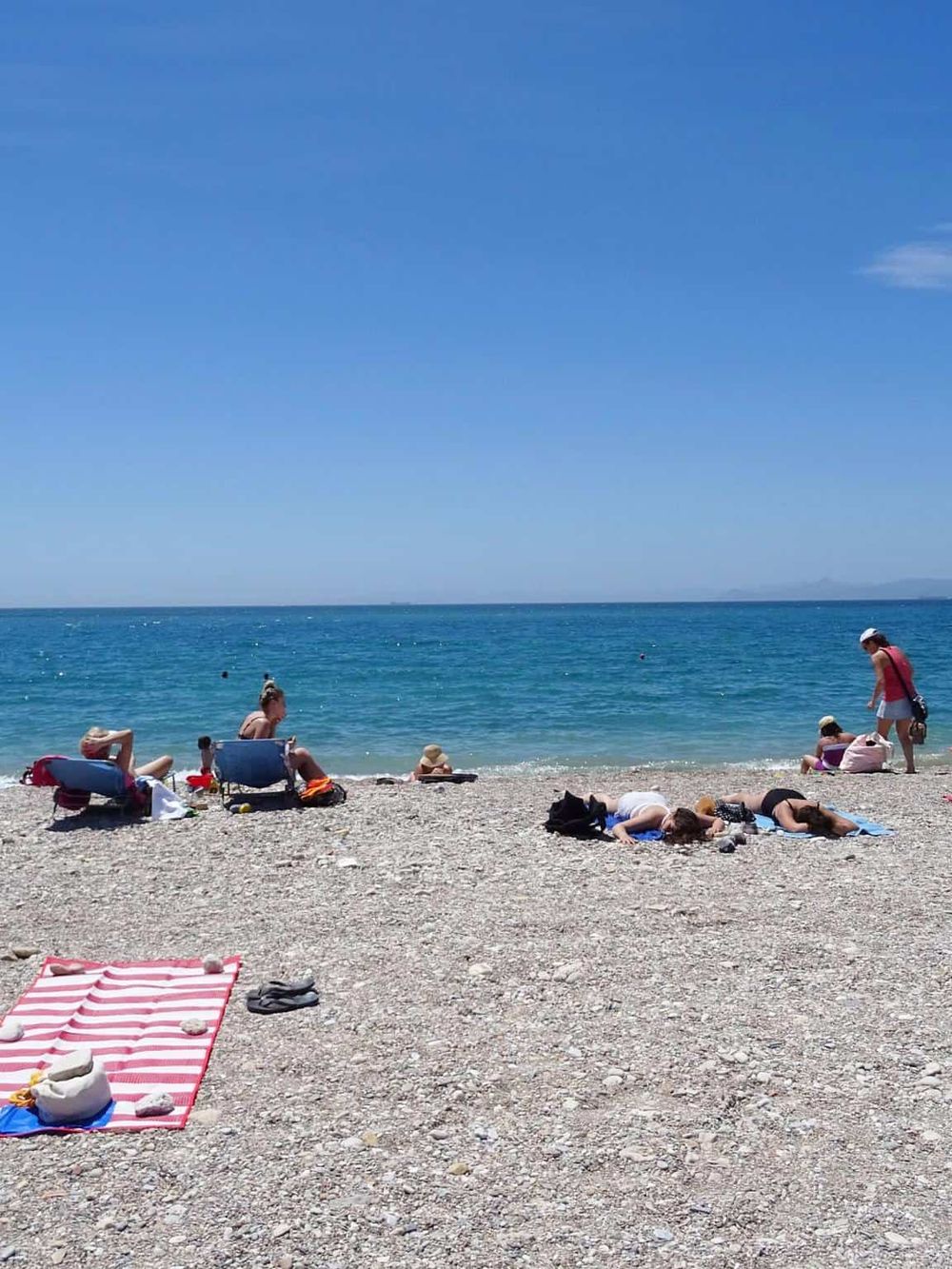 Beach scene with sunbathers, umbrellas, and clear blue water, showcasing scenic coastal views and relaxation.