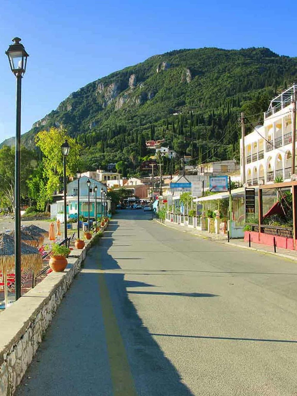 Scenic street view in a coastal mountain town with colorful buildings and lush green hillside.
