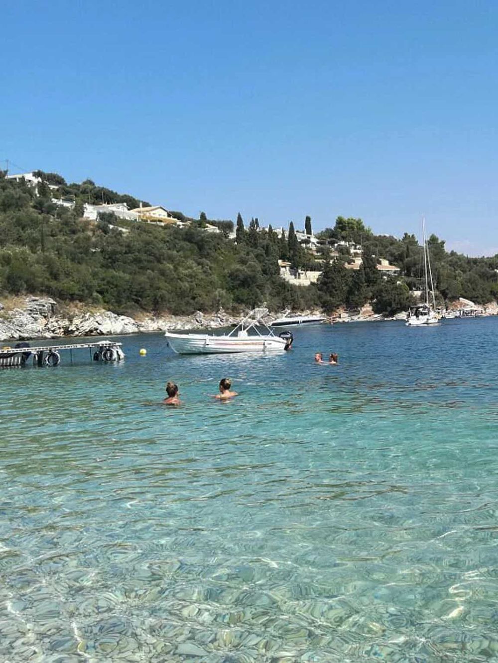 Tranquil seaside with clear waters, boats, and hillside homes, perfect for travel and leisure.