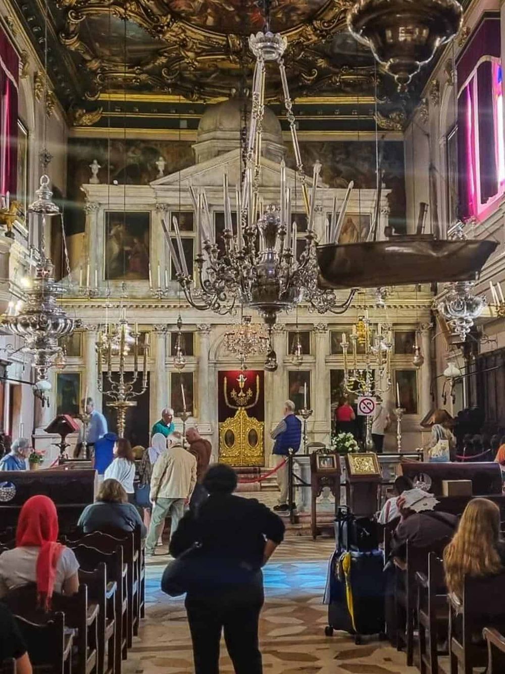 Intricate church interior with chandeliers and worshippers inside a historic religious site.