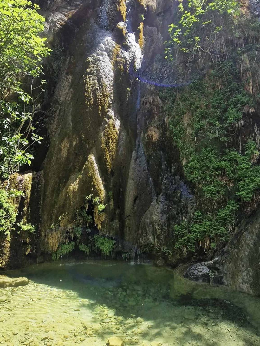 Serene waterfall in lush forest with clear pool, outdoor adventure, nature exploration, tranquil scenic spot.