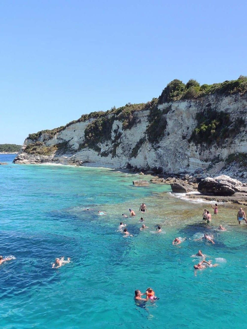 Brightly colored ocean swimmers enjoying a scenic coastal beach with rocky cliffs and turquoise water.