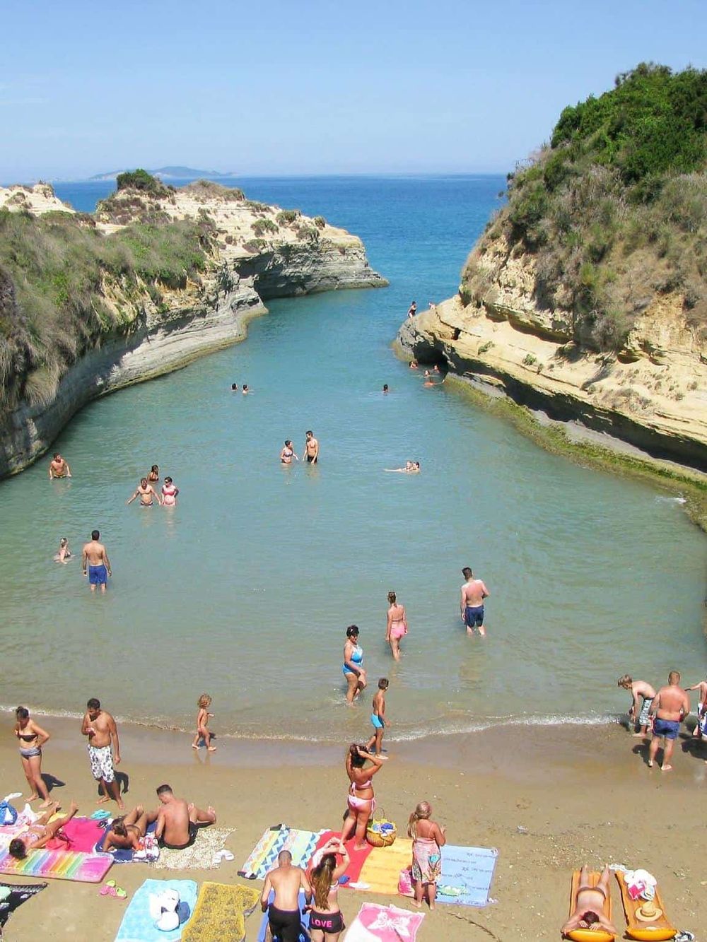 Hidden beach with turquoise water, cliffs, and visitors enjoying sunbathing and swimming. Perfect scenic destination for beach lovers.