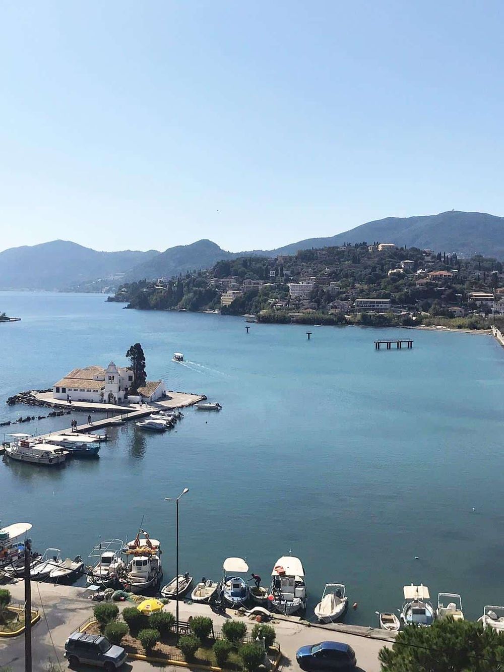 Calm lake with boats and a small church on a pier, surrounded by hills and scenic mountains.