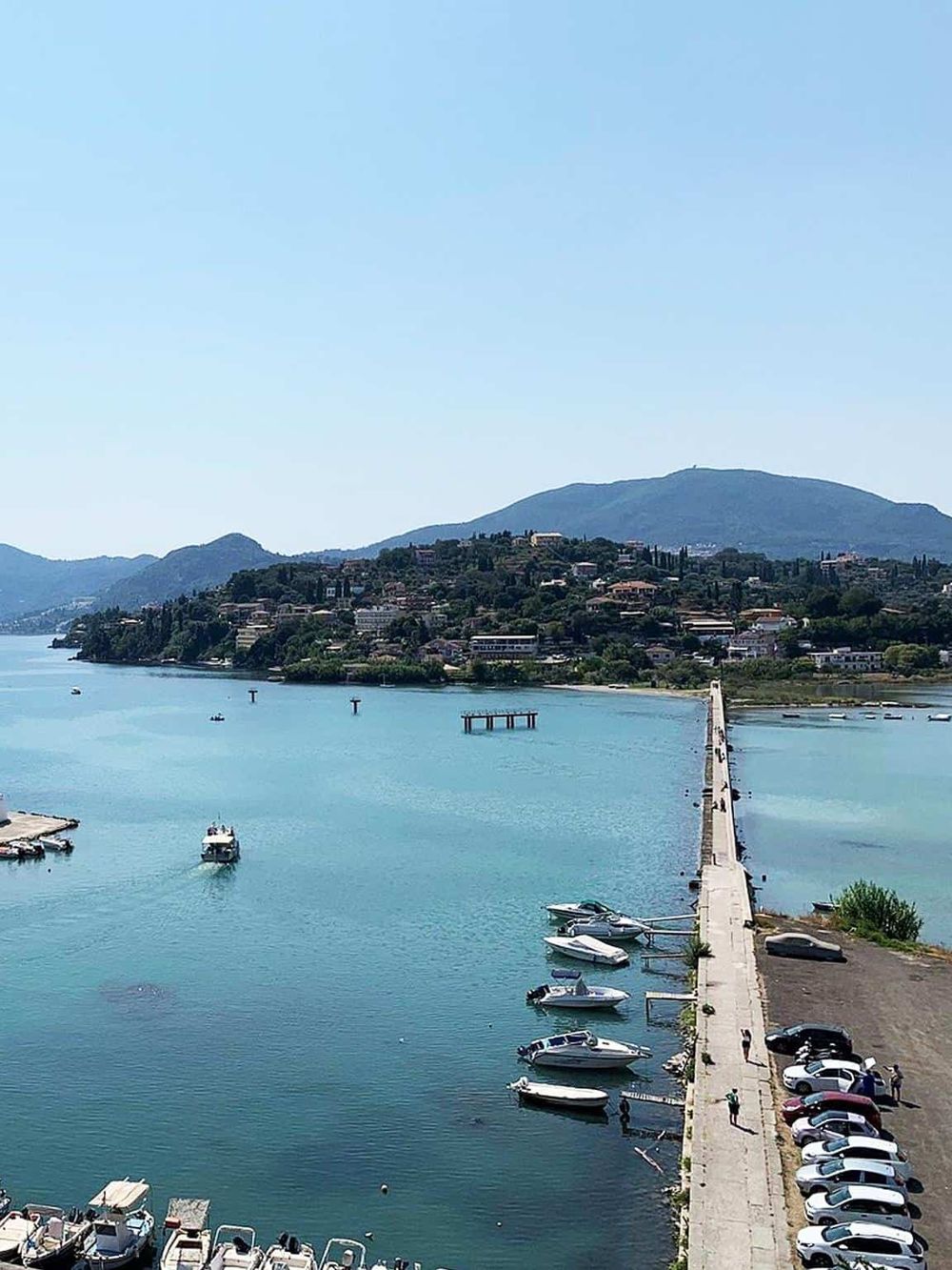 Aerial view of a serene lake with boats, coastline, and surrounding hills, highlighting scenic travel destinations.