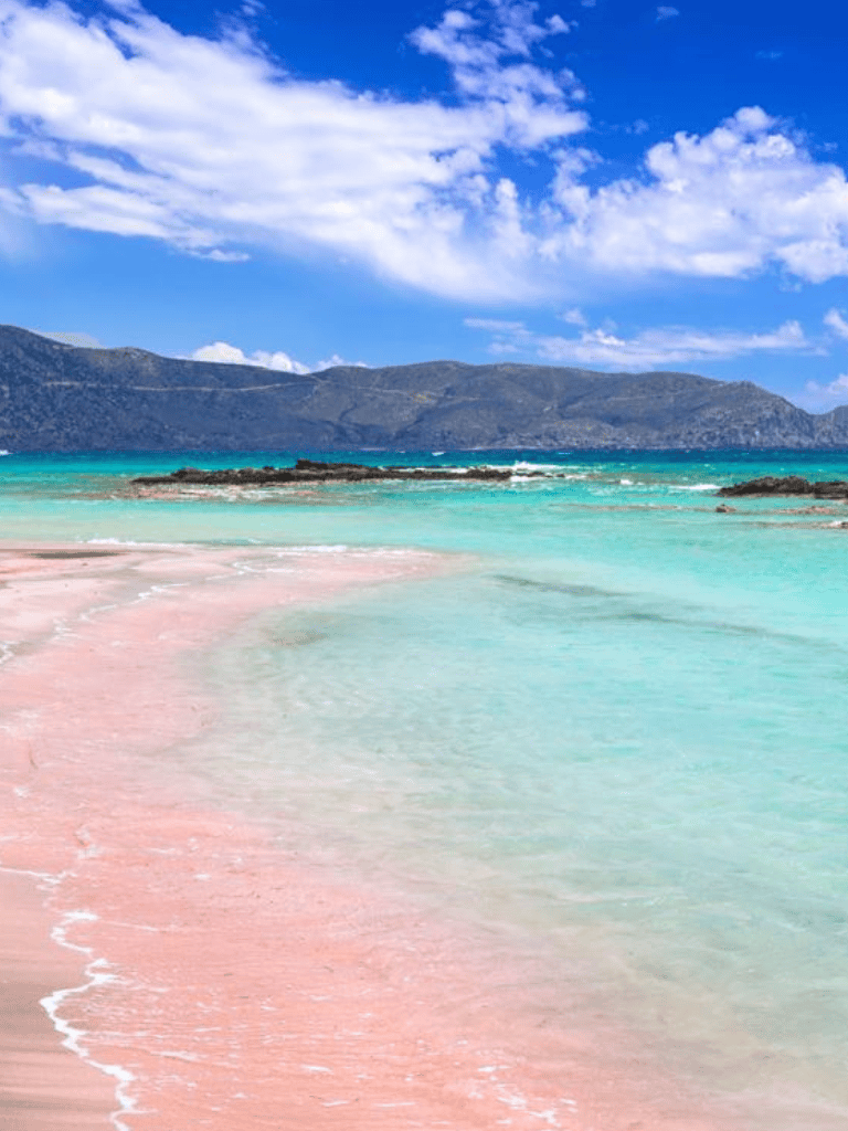 Pristine pink sand beach with turquoise waters and scenic mountain backdrop.