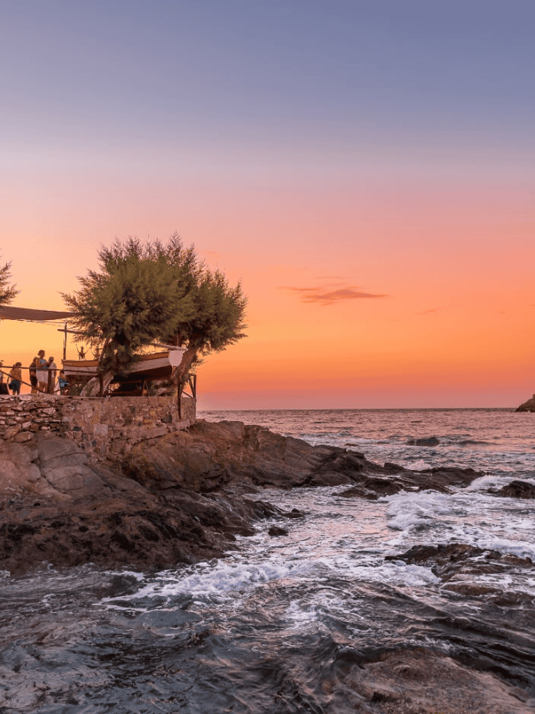 Sunset coastal view with rocky shoreline and people enjoying the evening scenery.