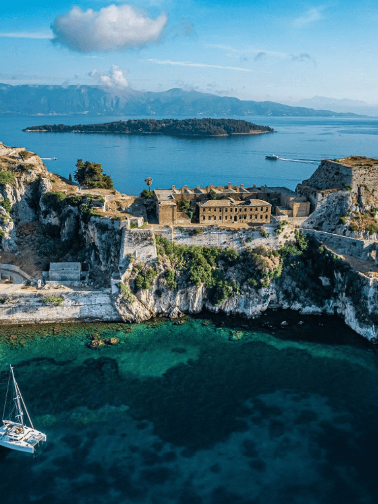 Spectacular coastal view of historic fortress overlooking blue sea and distant mountains.
