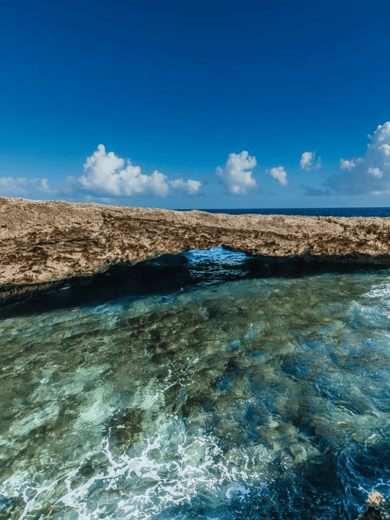 Vibrant coastal scene with natural rock arch and clear ocean water under a bright blue sky.