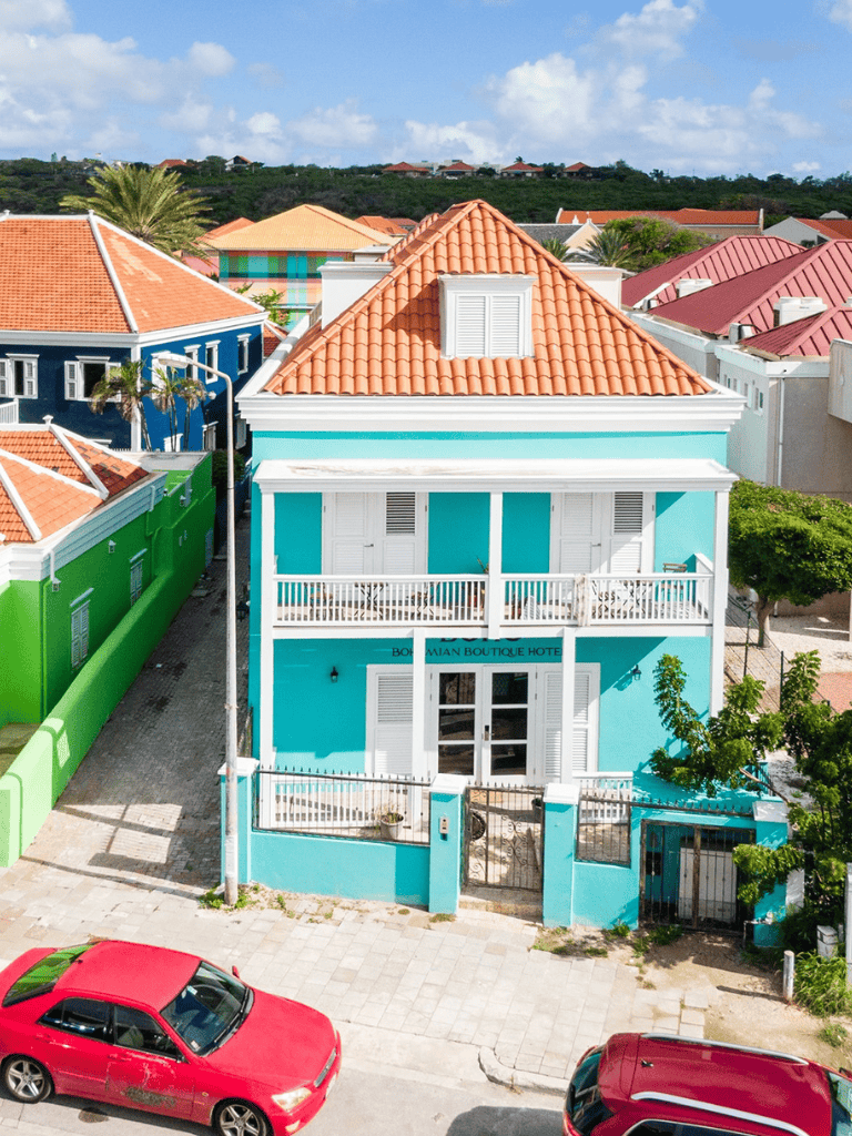 Vibrant turquoise boutique hotel with red-tile roof in colorful Caribbean neighborhood.
