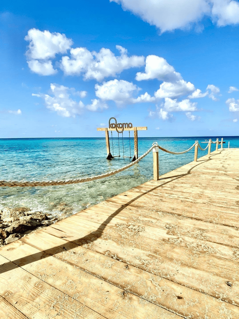Bright blue sky and clear turquoise ocean at Kokomo Cay, Curacao, with a wooden dock and swings over the water.