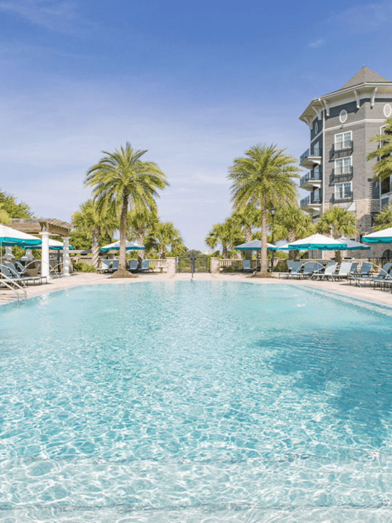 Relaxing resort pool with palm trees and modern building in the background, perfect for vacation and leisure.