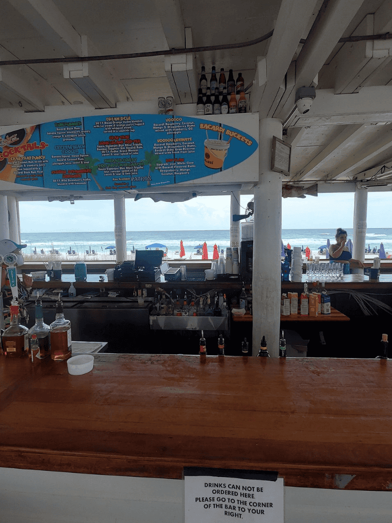 Beverage bar at beachside restaurant with ocean view and colorful drink menu, perfect for relaxing seaside dining.
