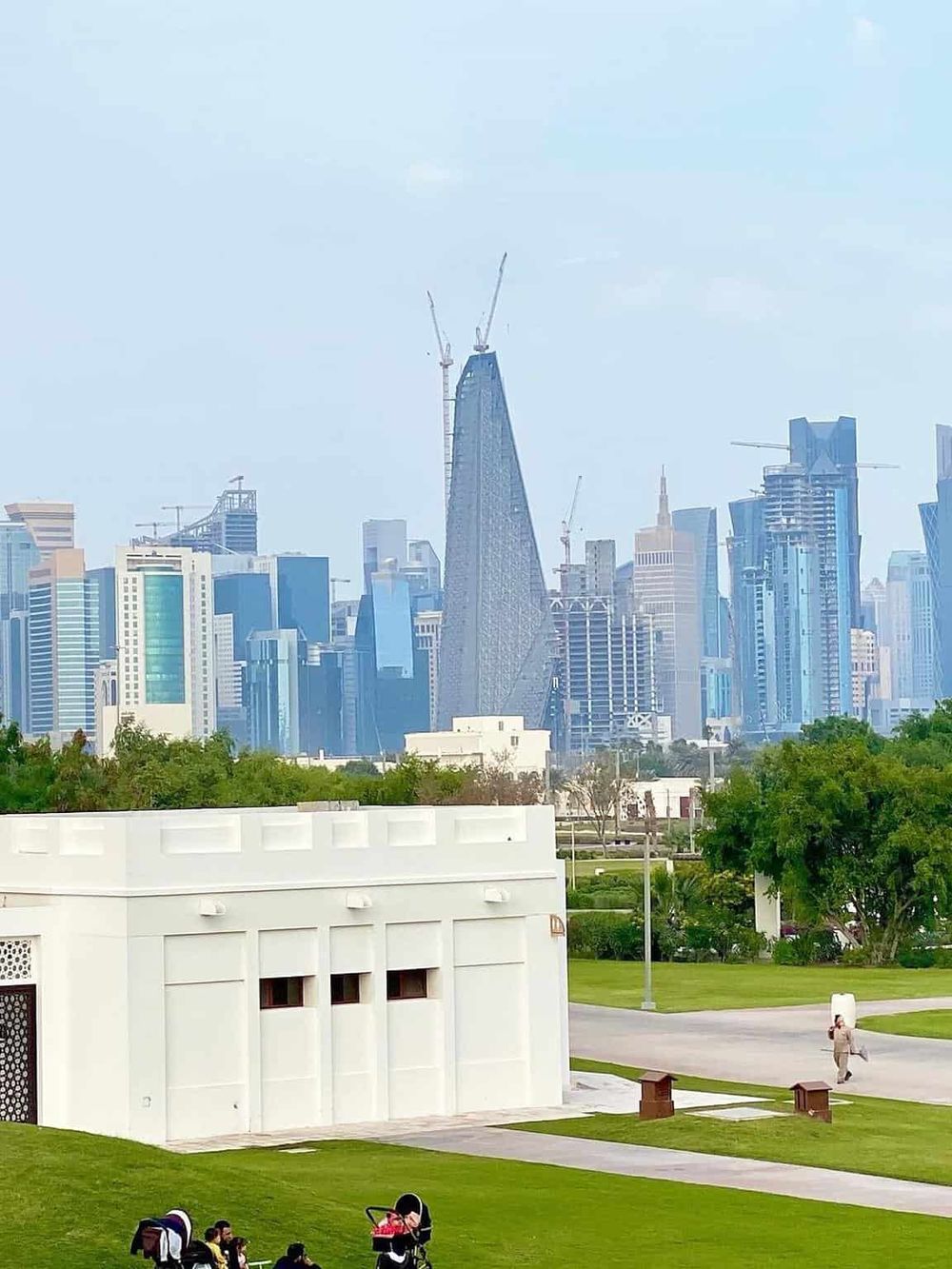 Modern city skyline with skyscrapers under construction, urban parks, and people enjoying outdoor activities.