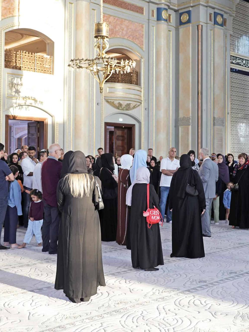 Colorful mosque interior with diverse group of people during tour or prayer session, showcasing architecture and cultural diversity.