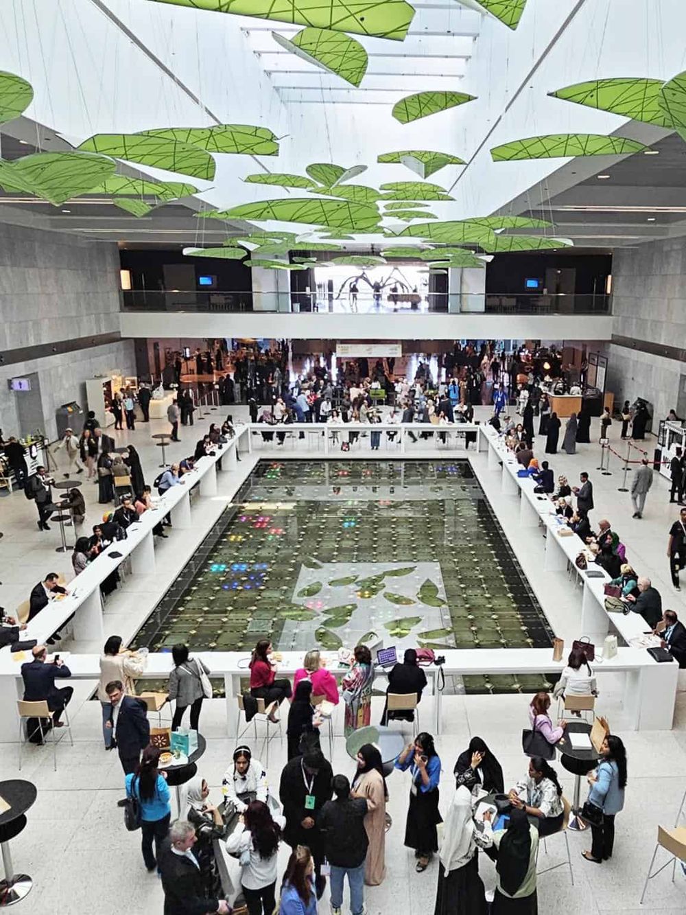 Bright, modern airport terminal with lush green ceiling art, busy travelers, and a large water feature.
