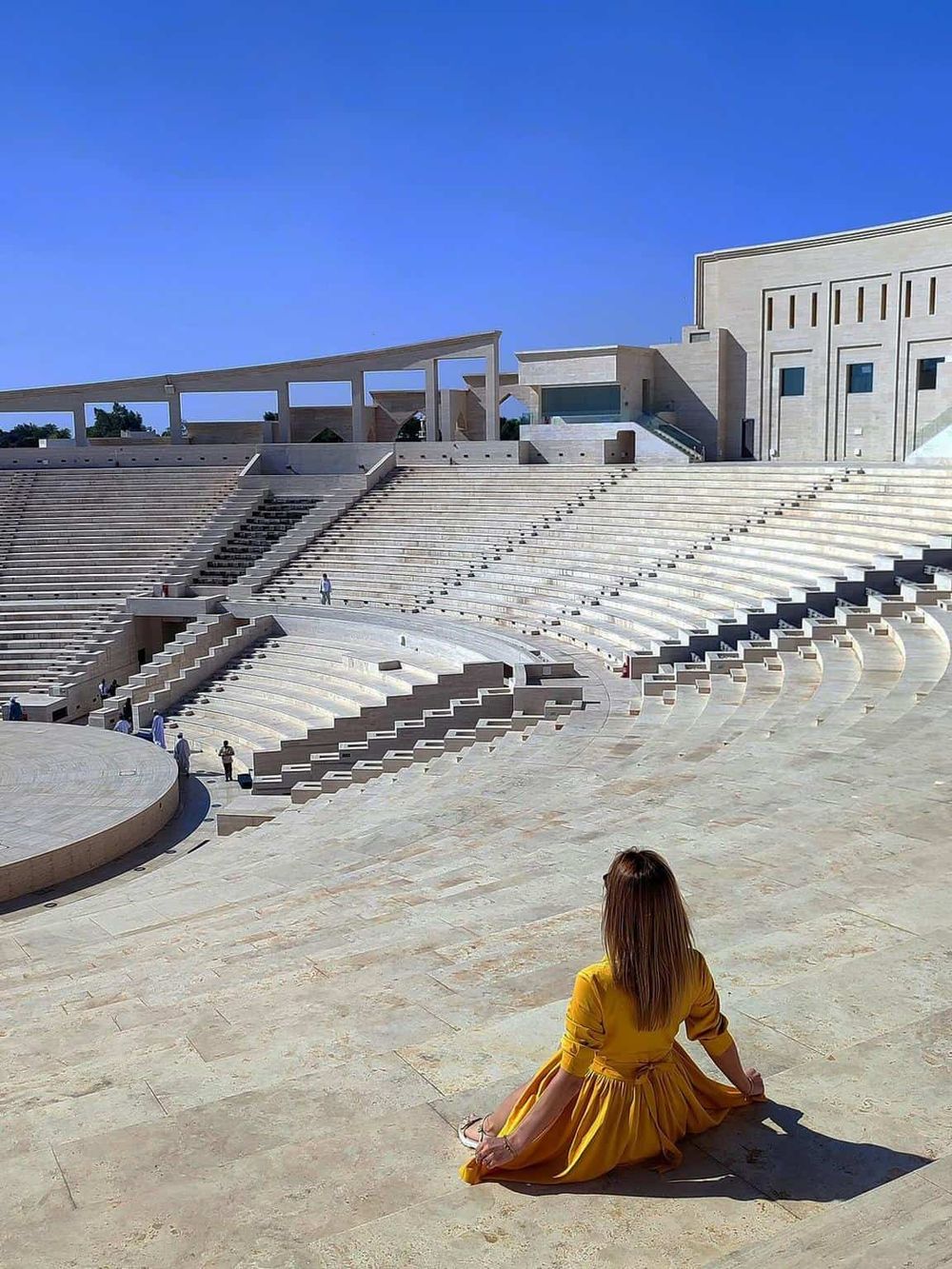 Serene woman in yellow dress sitting at the ancient Roman amphitheater, exploring cultural and historical landmarks.