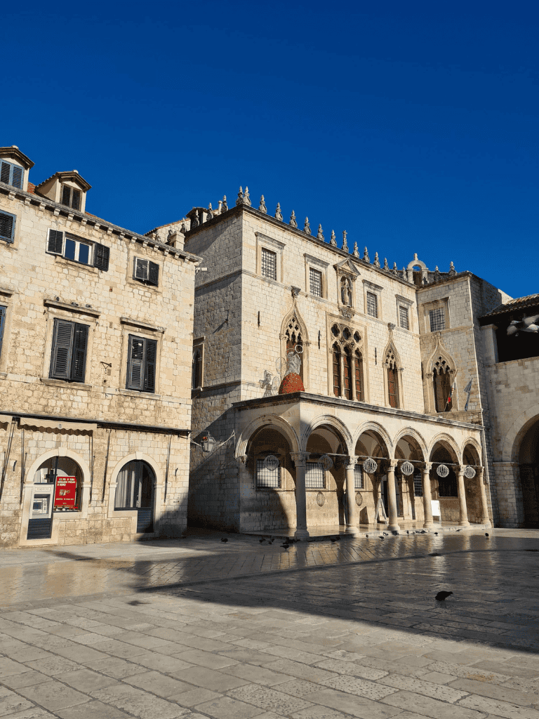 Ancient stone building with Gothic windows and arches in historic city center, sunny day.