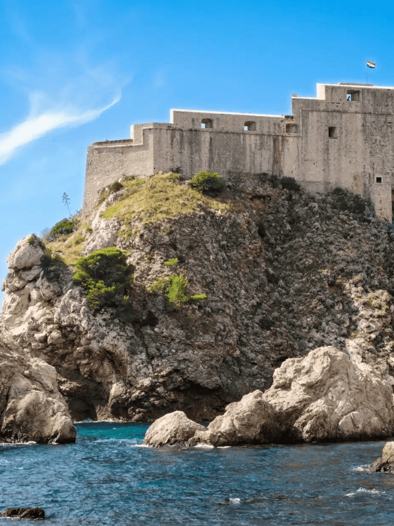 Ancient fortress on rocky coast overlooking blue ocean under clear sky.