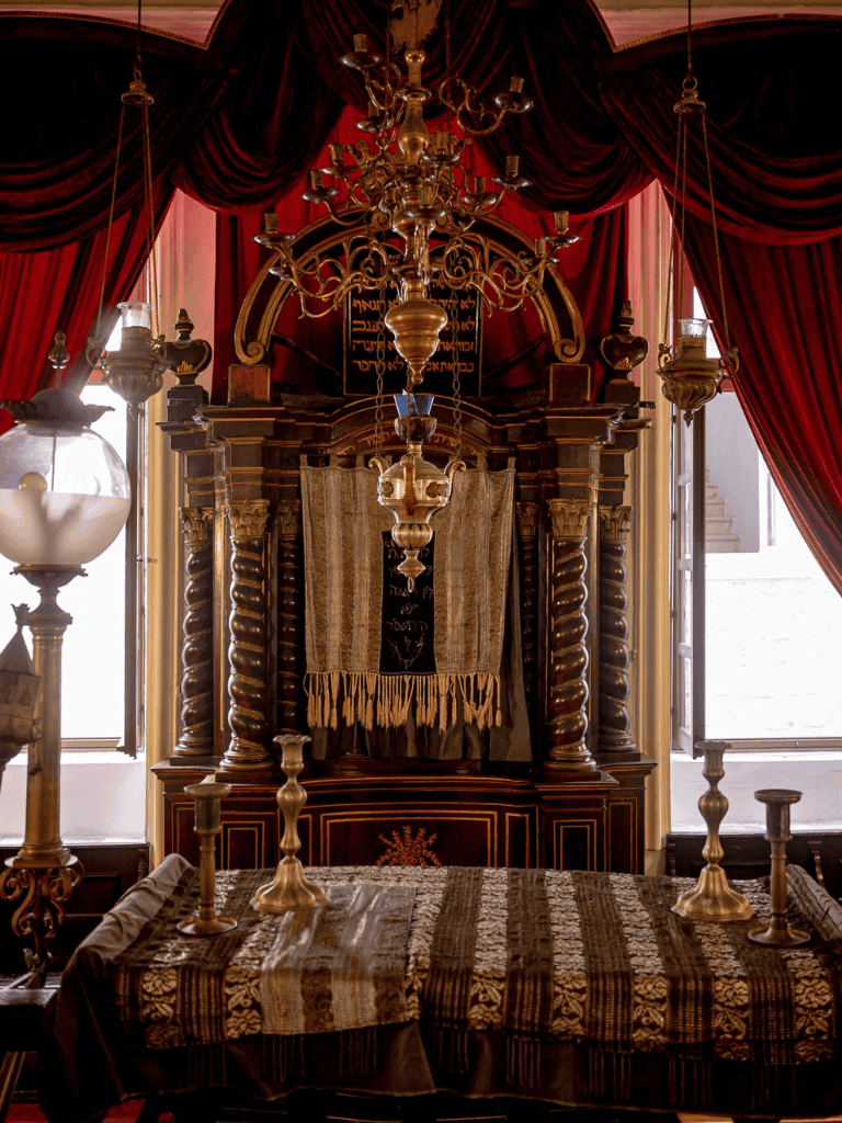 Ornate synagogue interior with wooden ark, chandelier, and red velvet curtains for religious worship.