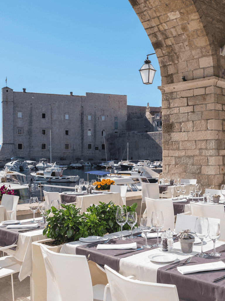 Harborfront outdoor restaurant with elegant dining setup in a historic port city.