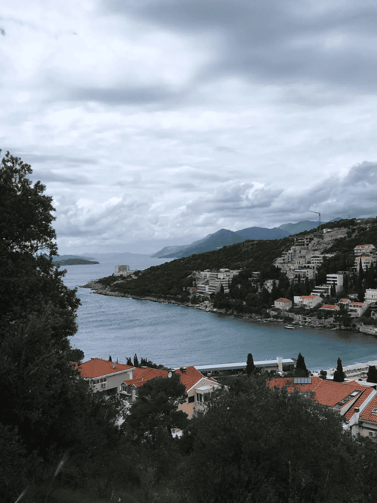 Serene coastal view with hillside houses and lush greenery under cloudy sky, ideal for travel inspiration.