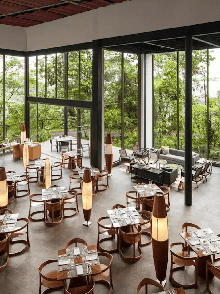 Elegant restaurant interior with floor-to-ceiling windows and lush greenery views.