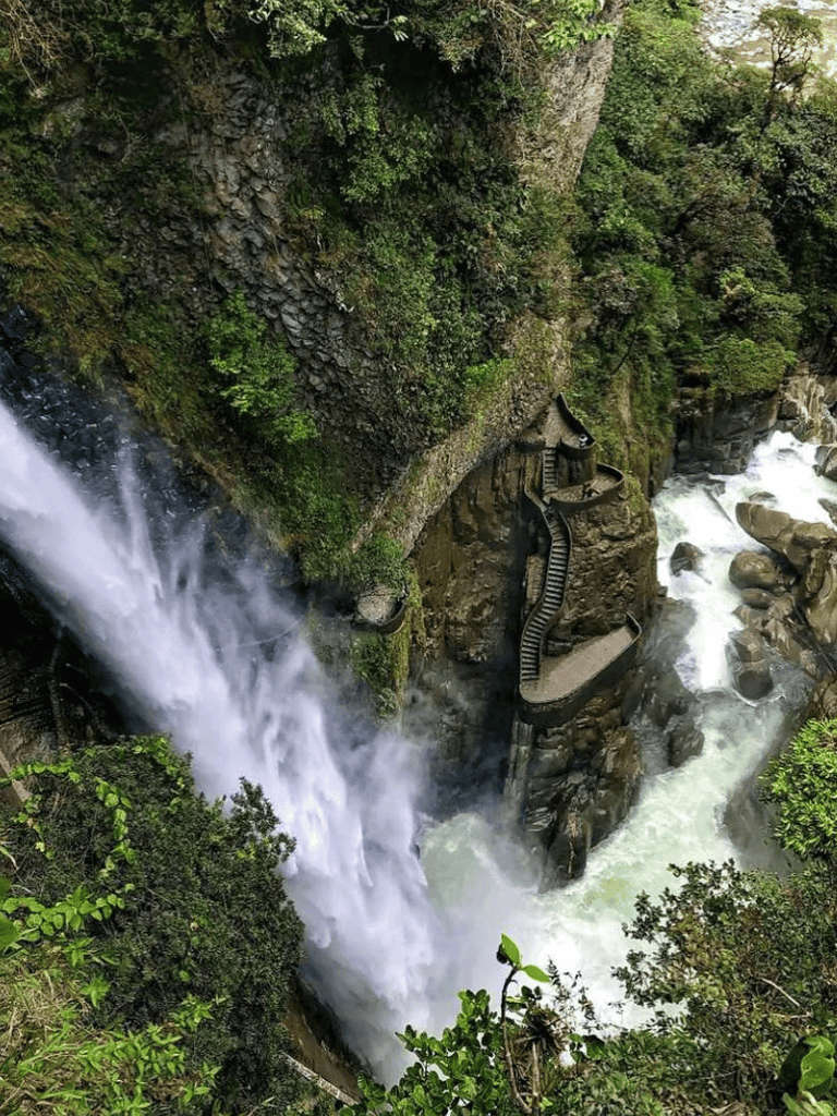 Cliffside waterfall with a winding staircase overlooking rushing river water.