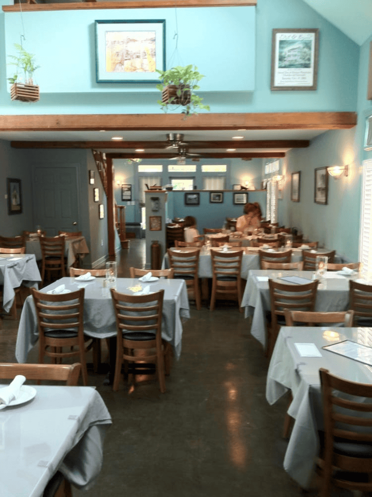 Cozy restaurant interior with wooden chairs, white tablecloths, and soft lighting.
