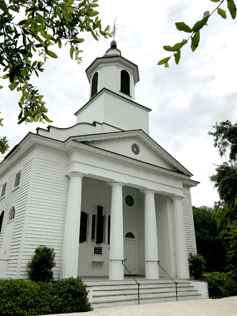 White historic church with classical columns and steeple in lush greenery, Georgia, USA.