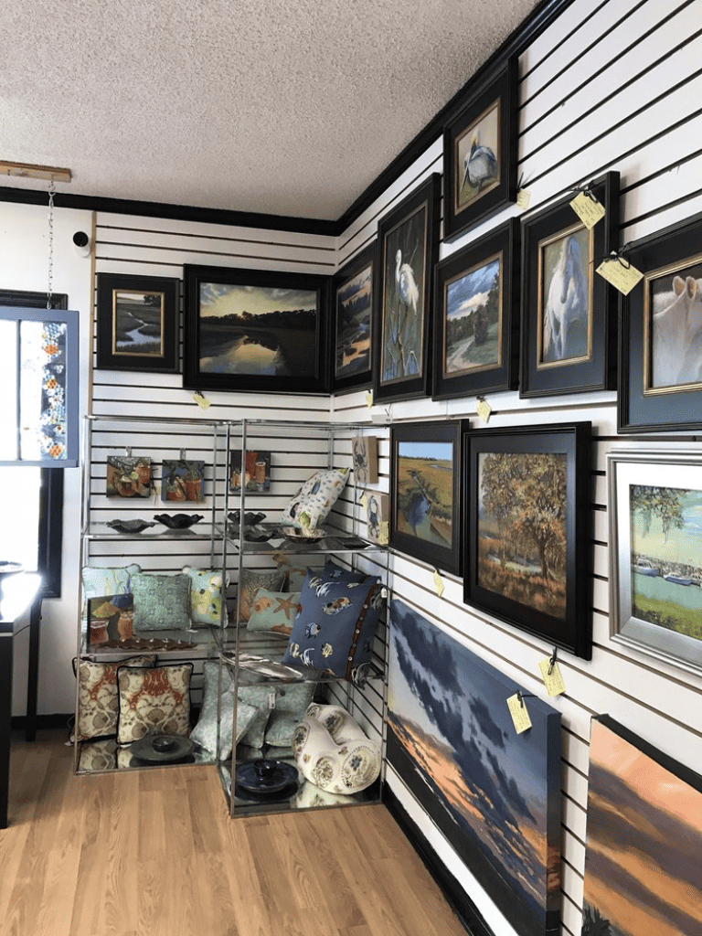Colorful landscape and animal paintings displayed in an art gallery or shop.