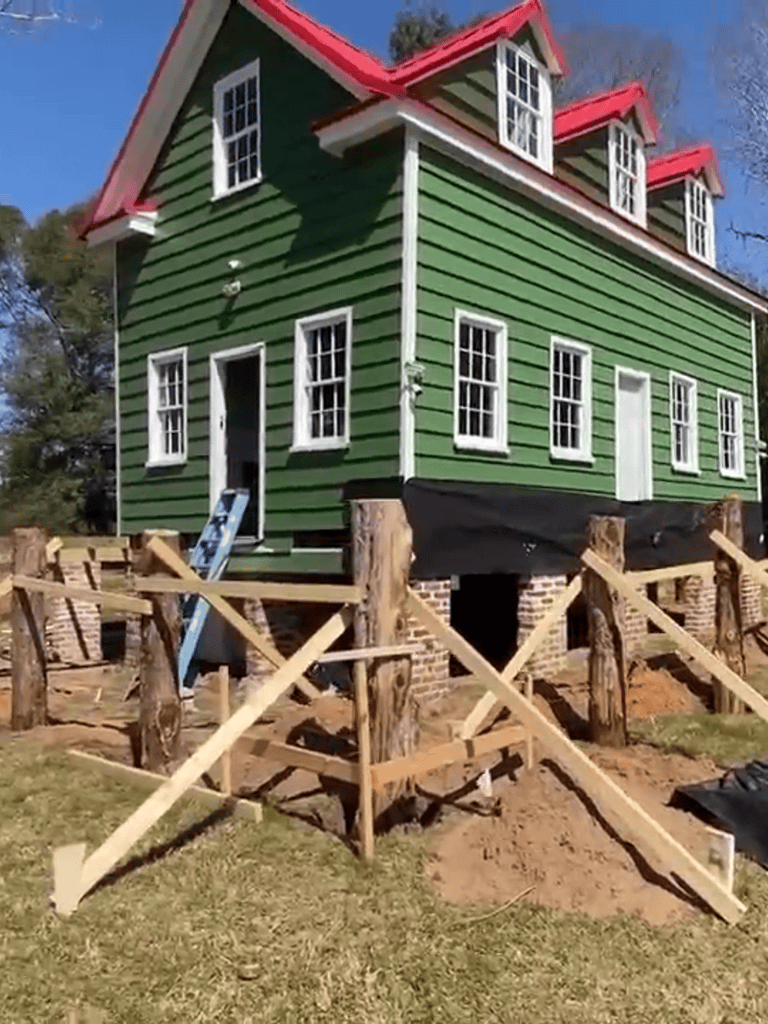 Colorful green house with red roof under construction, wooden support posts and scaffolding.