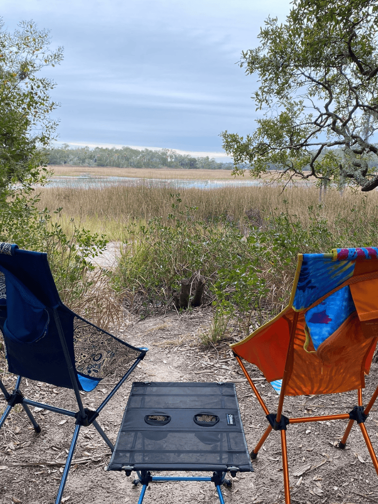 Secluded marshland view with two camping chairs and a small foldable table by the water.