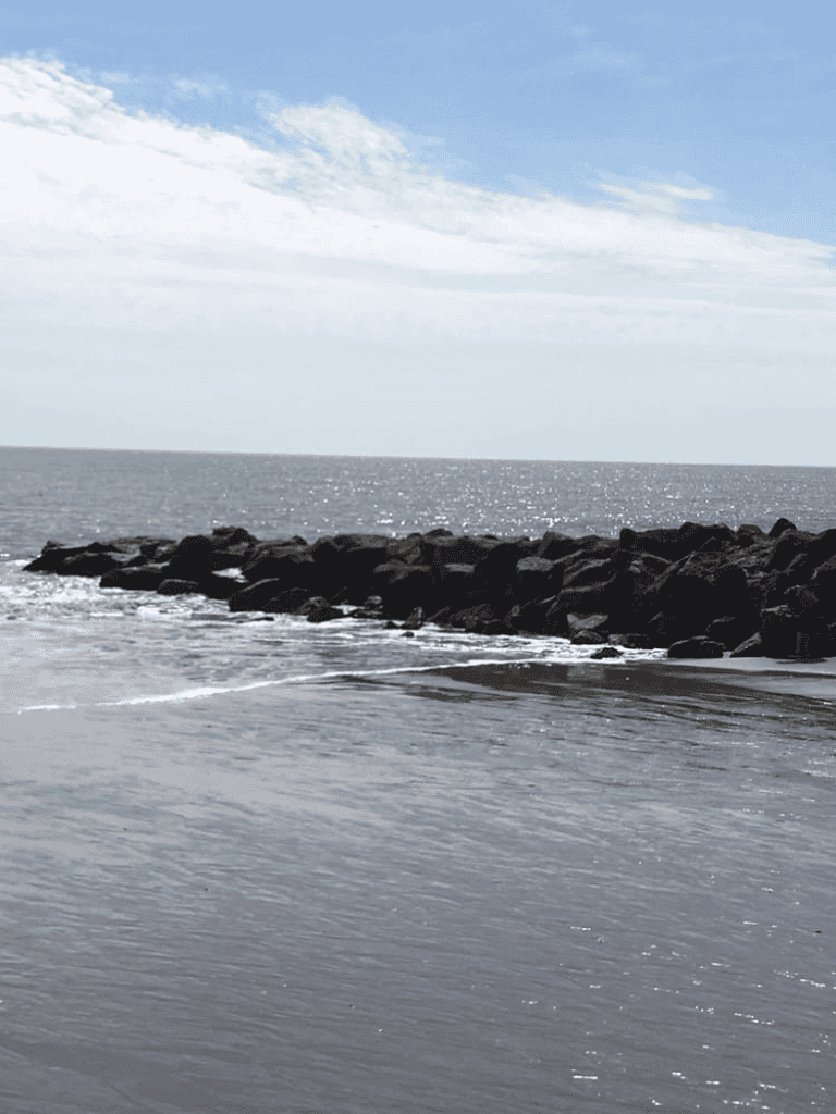 Serene beach scene with rocks, ocean waves, and clear sky in the background, ideal for travel and coastal exploration.