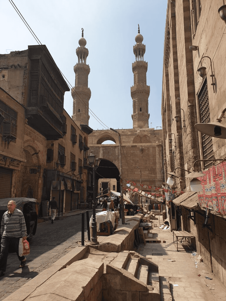 Ancient Middle Eastern street view with minarets, traditional buildings, and market stalls.