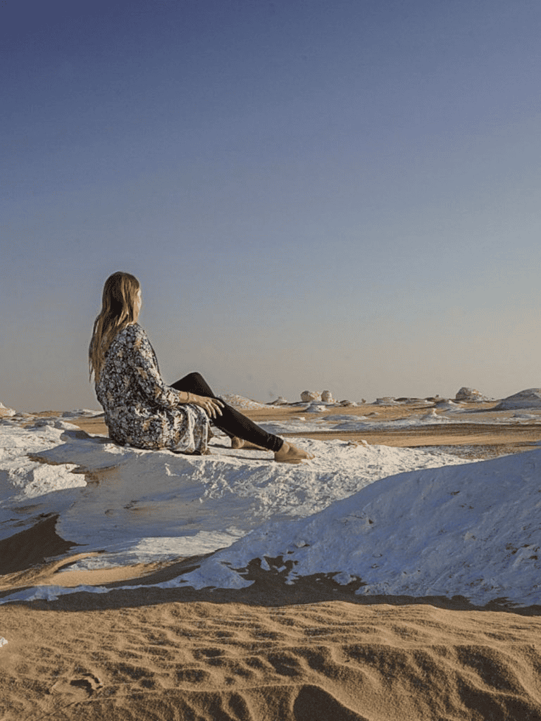 Peaceful woman sitting on white rocks in desert landscape at sunset, exploring natural beauty.