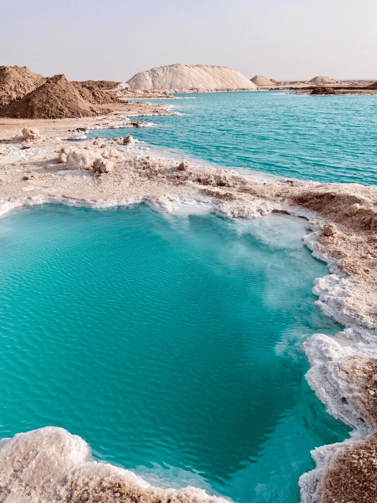 Vivid turquoise hot springs in a desert landscape with mineral deposits and salt formations.