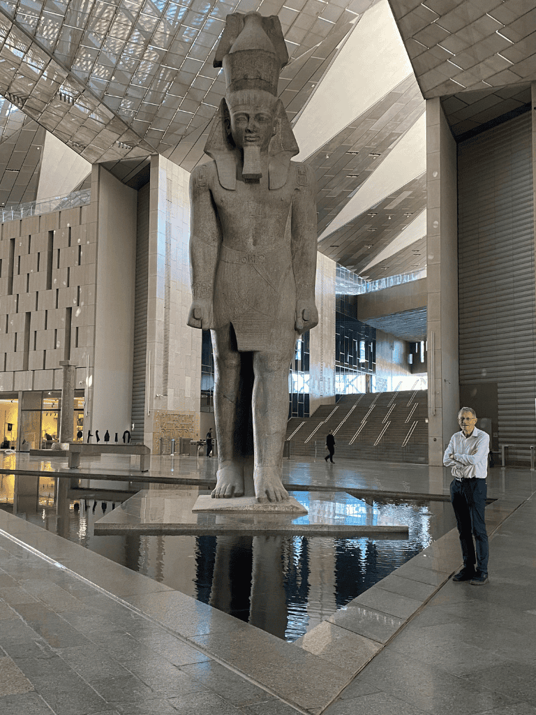 Ancient Egyptian sculpture of Pharaoh towering inside a modern building with reflective water pool.