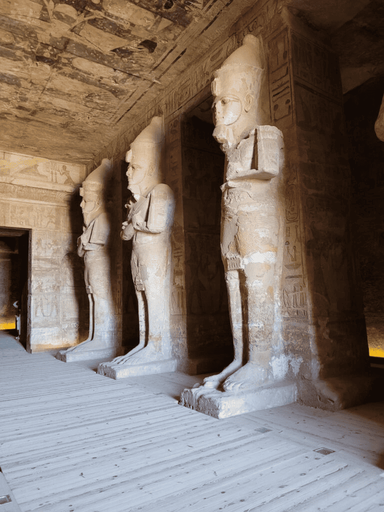 Ancient Egyptian statues in a historic temple with hieroglyphics on walls.