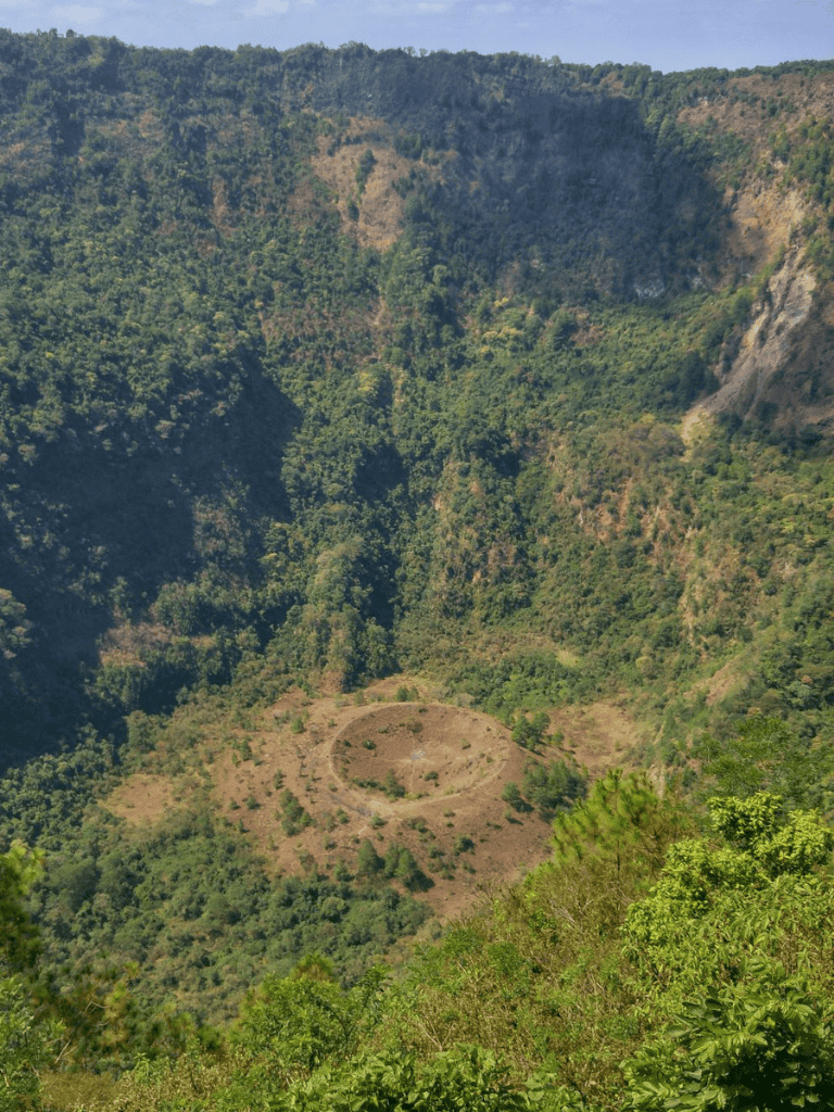 Ancient crater surrounded by lush greenery in a scenic mountain landscape.