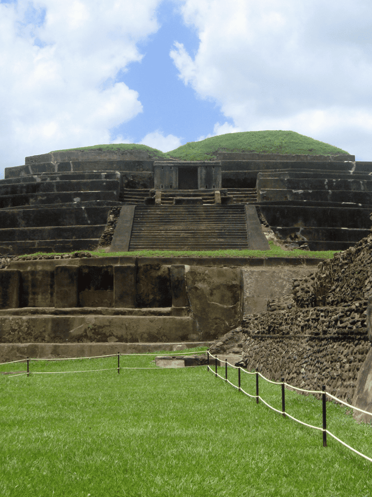 Ancient Mesoamerican pyramid with steps and lush green surroundings on a clear day.