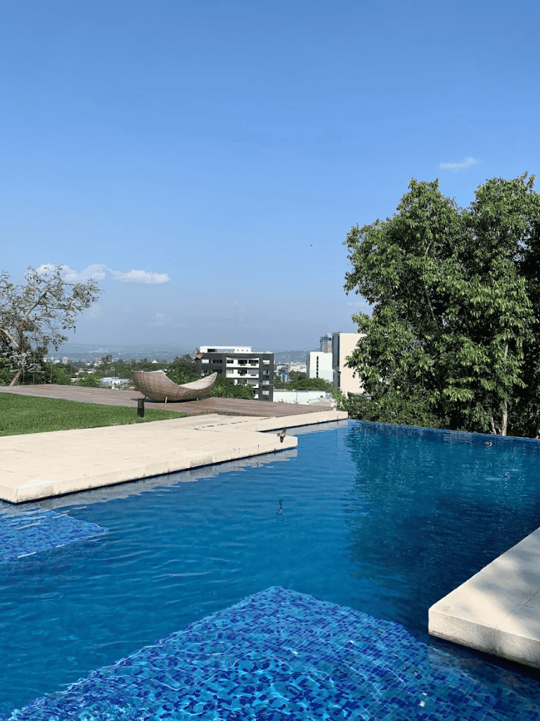 Luxurious rooftop infinity pool with city views and lush greenery in the background.