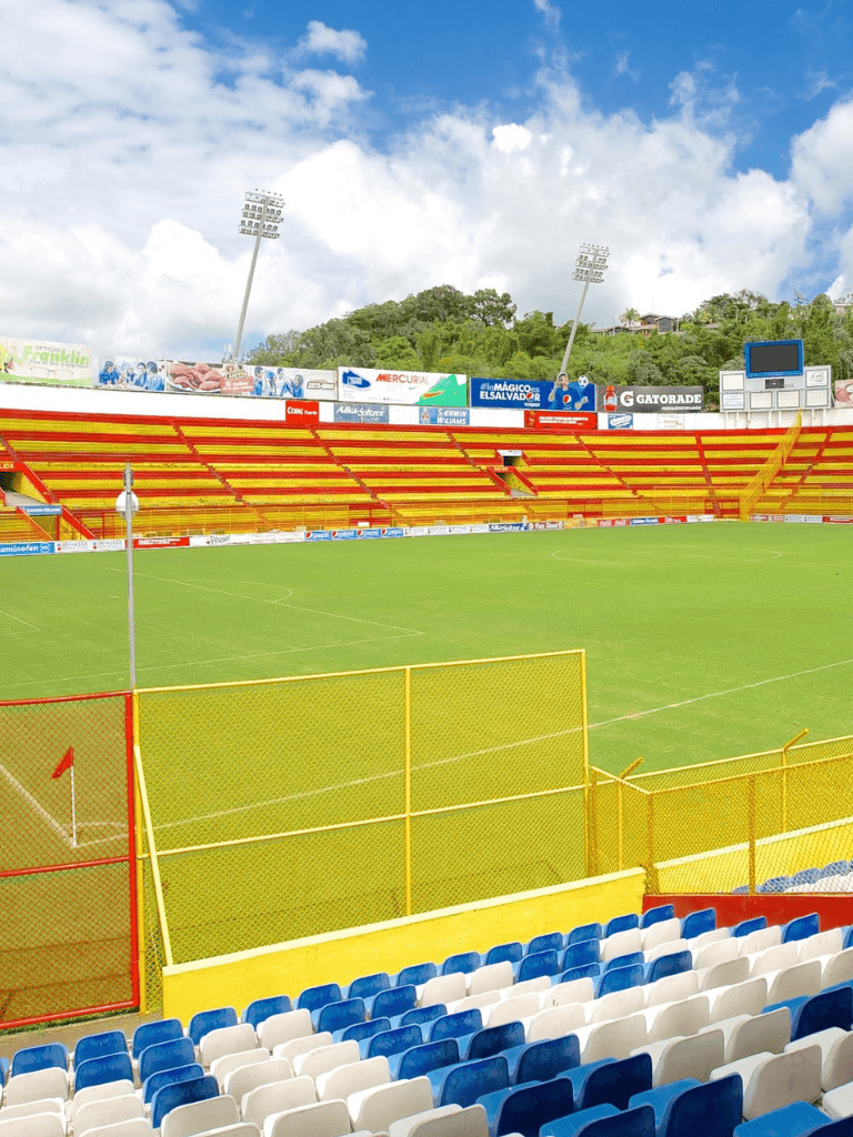 Soccer stadium with vibrant red and yellow seating, lush green field, and clear sky; ideal for soccer events and sports fans.