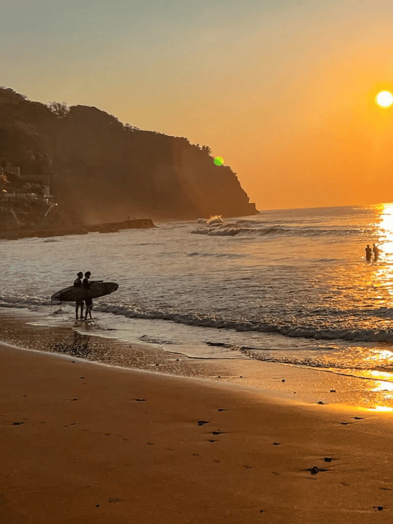 Serene beach sunset with surfers and coastal cliffs, perfect for beach destinations.