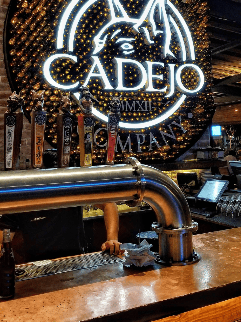 Neon Cadejo logo at a bar with craft beer taps in the background.