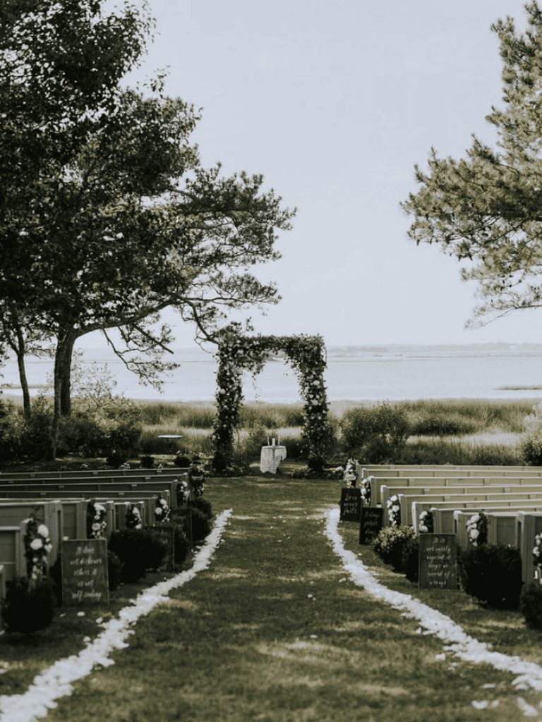 Charming outdoor wedding setup by the water with floral decorations and elegant chairs, perfect for seaside ceremonies.
