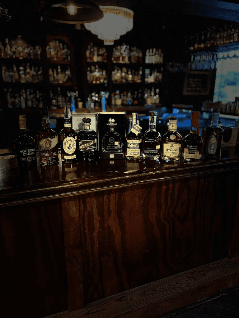 Whiskey bottles on bar counter at cozy tavern, extensive spirit collection for whiskey enthusiasts.